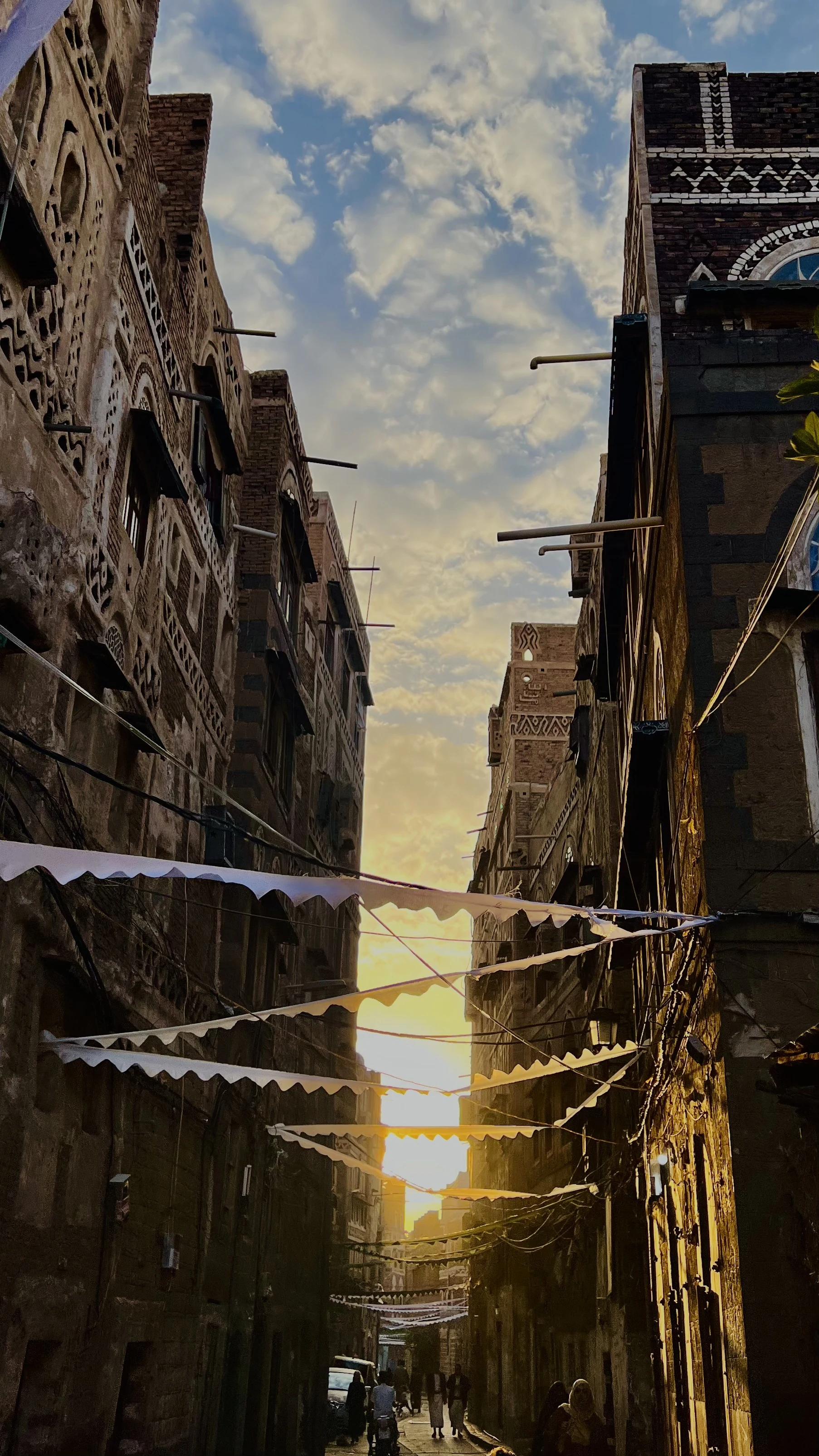 Narrow alley in an old walled city at sunset, ornately decorated multi-story buildings lined with triangular bunting flags