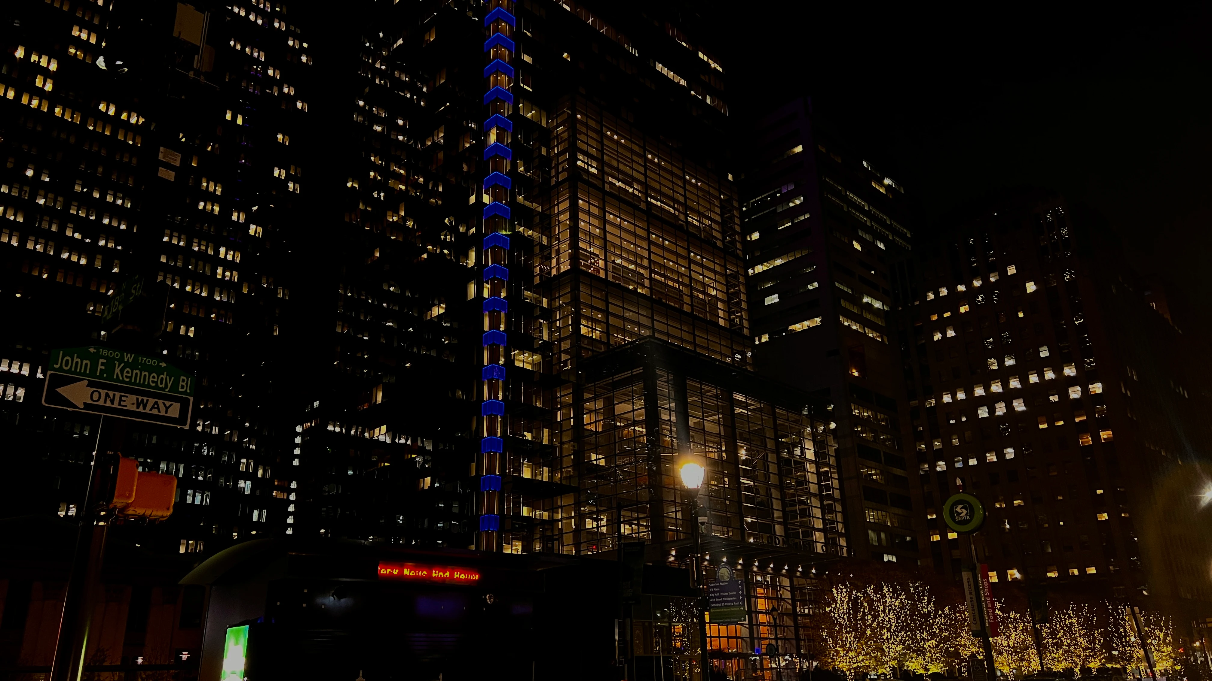 Night view up a cluster of illuminated skyscrapers on John F. Kennedy Boulevard, blue accent lights tracing one tower's facade