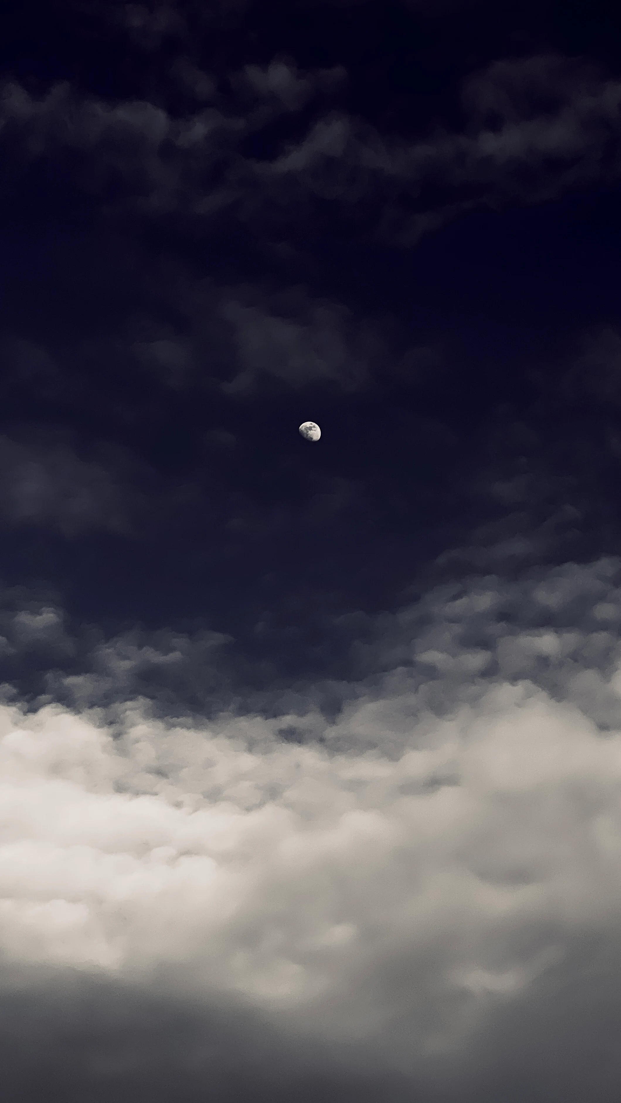 A gibbous moon glowing faintly through wispy dark clouds in a moody night sky
