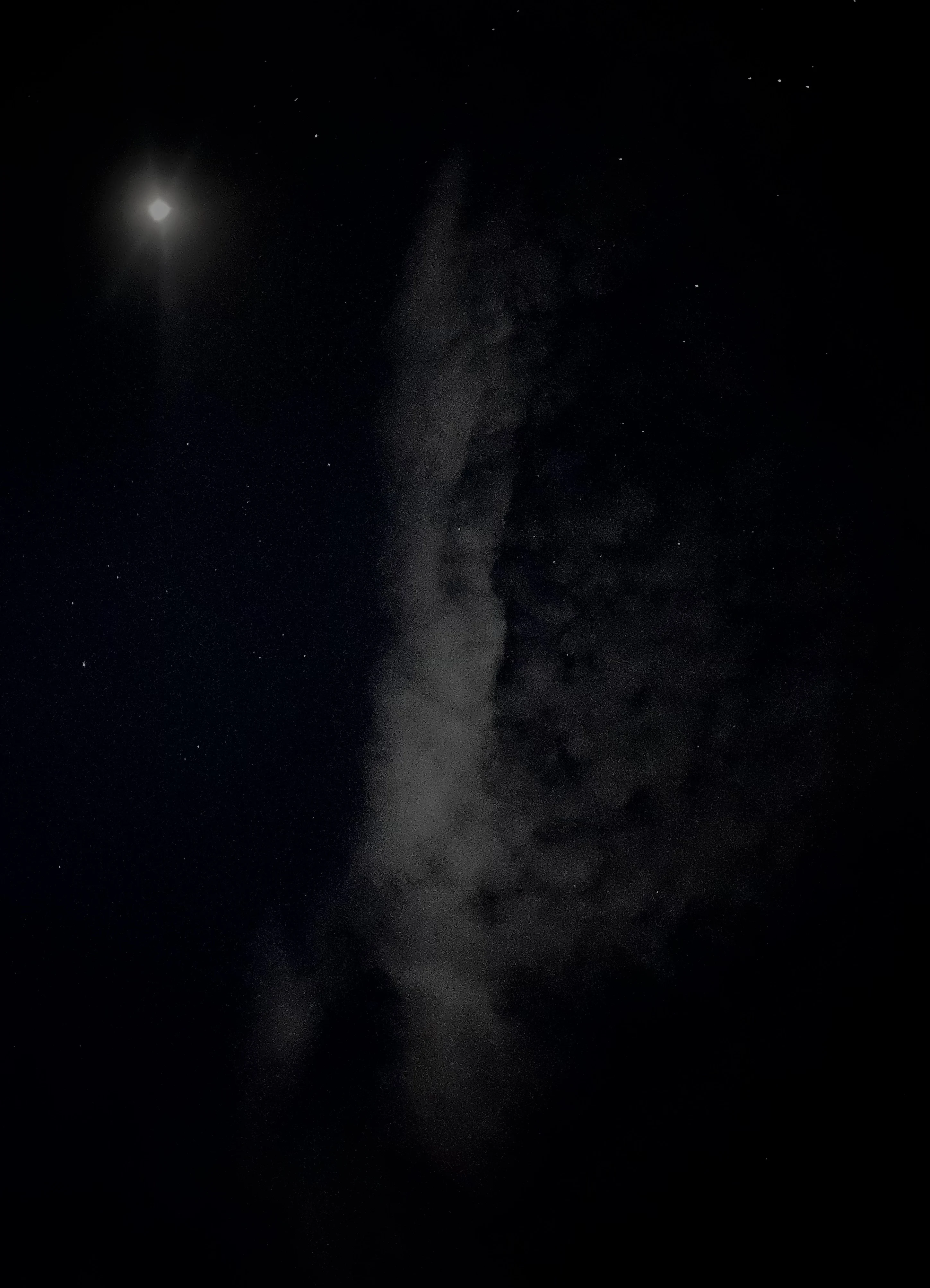 A bright moon flaring beside a wisp of cloud in a dark starry night sky